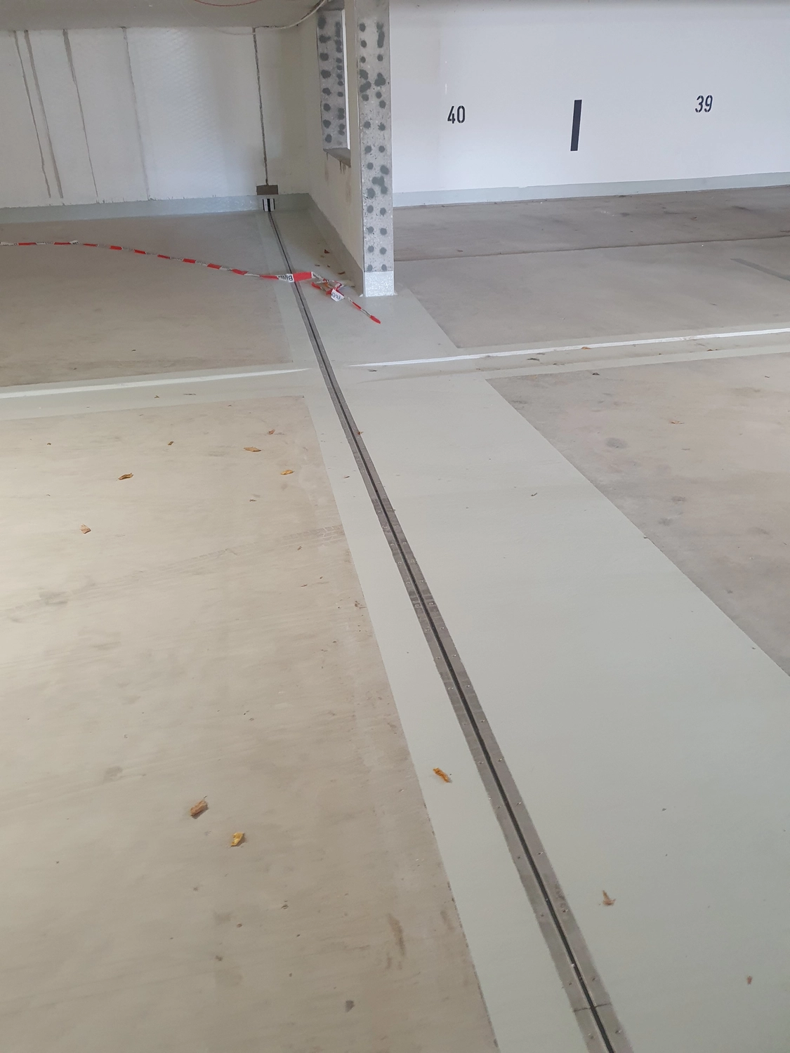 A&S Armbruster & Sieber GmbH - Experten im Bereich Bautenschutz und Bodenbeschichtungen - Leerer überdachter Parkplatz mit den Nummernplätzen 39 und 40 und einer sichtbaren Metalldehnungsfuge auf dem Betonboden
