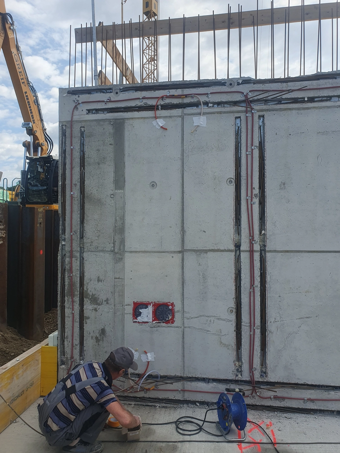 A&S Armbruster & Sieber GmbH - Experten im Bereich Bautenschutz und Bodenbeschichtungen - Bauarbeiter kauert neben einer Betonwand mit freiliegenden Elektroleitungen und Leitungen auf einer Baustelle