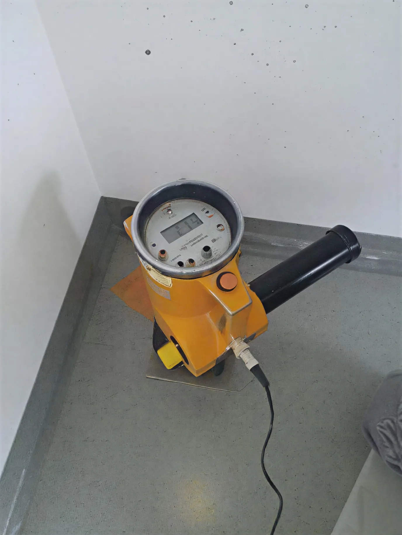 A&S Armbruster & Sieber GmbH - Experten im Bereich Bautenschutz und Bodenbeschichtungen - Gelbes Handvermessungsgerät mit digitaler Anzeige der Zahl 719, platziert auf einem grauen Boden neben einer weißen Wand