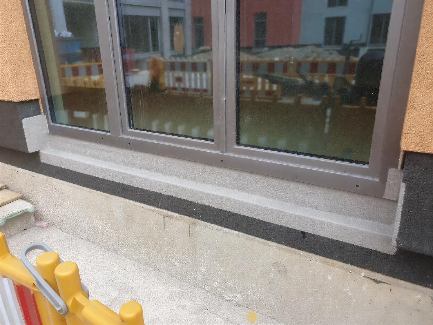 A&S Armbruster & Sieber GmbH - Experten im Bereich Bautenschutz und Bodenbeschichtungen - Nahaufnahme eines Fensters mit grauem Rahmen an einer Gebäudewand, auf dem sich Bauhindernisse im Glas spiegeln