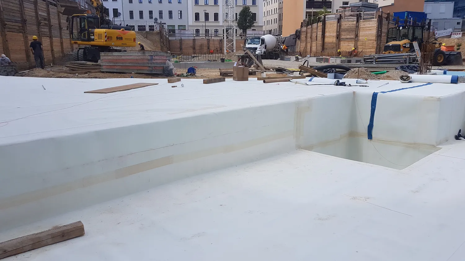 A&S Armbruster & Sieber GmbH - Experten im Bereich Bautenschutz und Bodenbeschichtungen - Baustelle mit einer großen weißen wasserdichten Membraninstallation, Baumaschinen und Arbeitern im Hintergrund