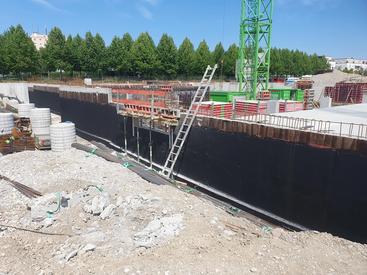 A&S Armbruster & Sieber GmbH - Experten im Bereich Bautenschutz und Bodenbeschichtungen - Baustelle mit Betonfundamentwänden, die mit schwarzem Abdichtungsmaterial beschichtet sind, und einer an der Wand gelehnten Metallleiter